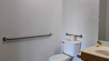 Een badkamer met een wit toilet, een handgreep, een wastafel met spiegel en een afvalbak.