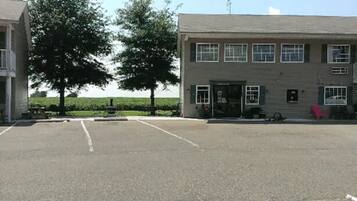 A parking lot with a building that has multiple windows and a door. There are trees and a clear sky in the background.