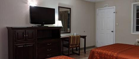 A hotel room with two beds, a TV, a desk, a chair, and a door marked "EXIT".