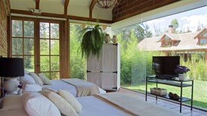 Ein Schlafzimmer mit zwei Betten, einem Fernseher auf einem Schrank und Blick auf ein Haus durch große Fenster.