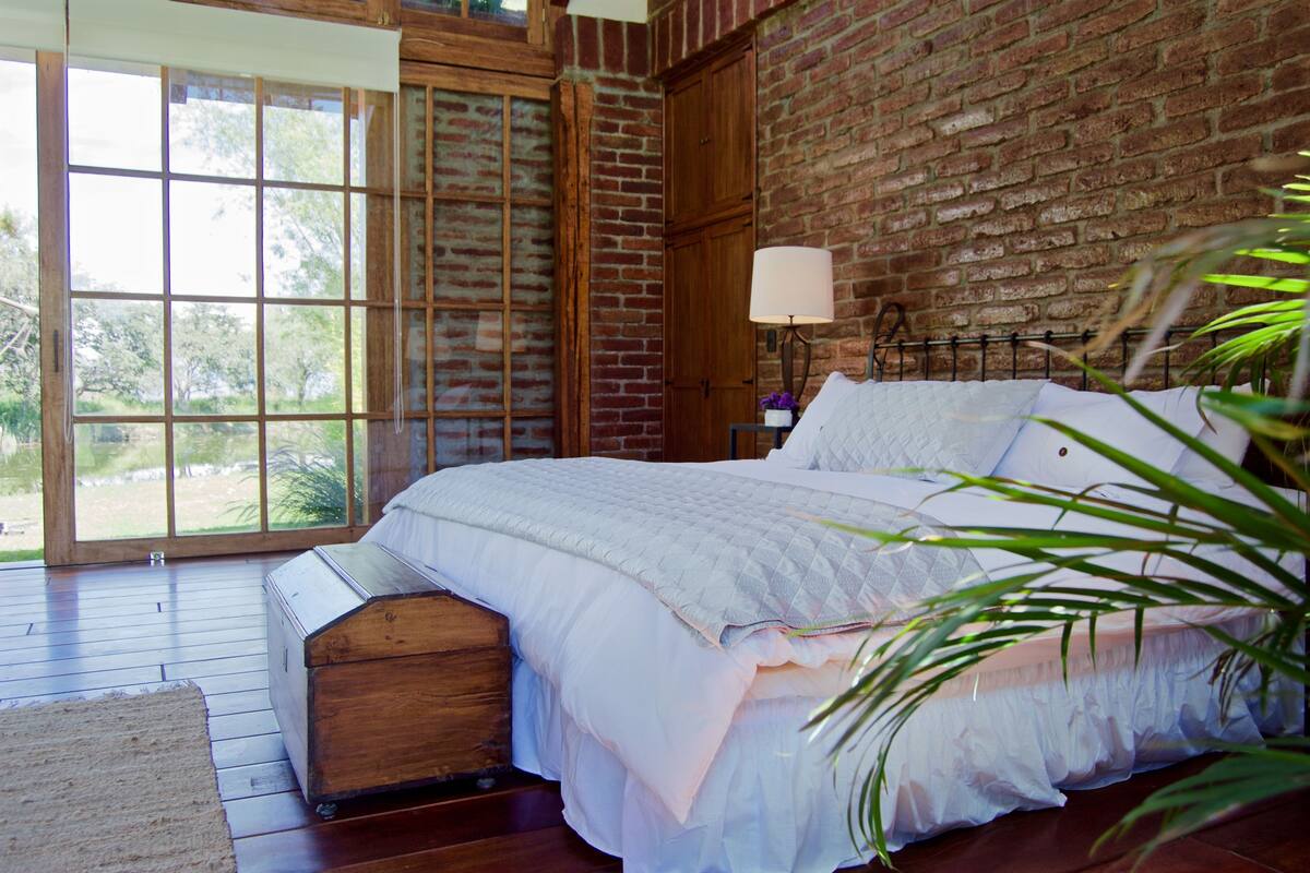 Een slaapkamer met een groot bed, houten vloeren, een bakstenen muur en een raam.