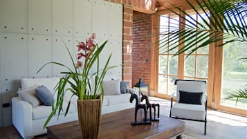 Una sala de estar moderna con un sofá blanco, una mesa de centro de madera, esculturas decorativas de caballos y una planta grande en maceta.