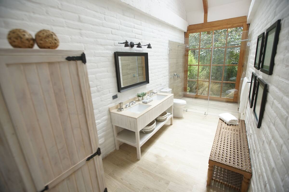 Een badkamer met een witte baksteenmuur, een houten bankje, een wastafel en een toilet.