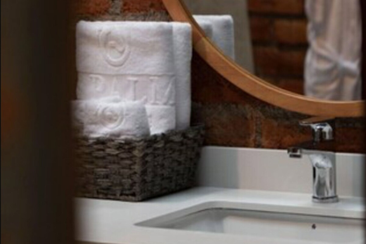 A bathroom with a white sink, a round mirror, and a brick wall.
