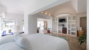 A spacious bedroom with a large bed, a television on a shelf, and a view of the outdoors.