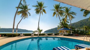 A poolside area with lounge chairs, a clear blue pool, palm trees, and a view of the sea and hills. - Exclusiva Villa Aldila frente al mar en Acapulco (Acapulco)
