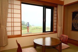 A room with a wooden table and chairs, a view of the sea through a window with a grid pattern, and a poster on the wall. - Hotel Tappi (Sotogahama)