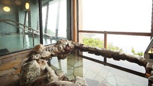 A stone wall with a wooden railing overlooking a pool area. - Hotel Tappi (Sotogahama)