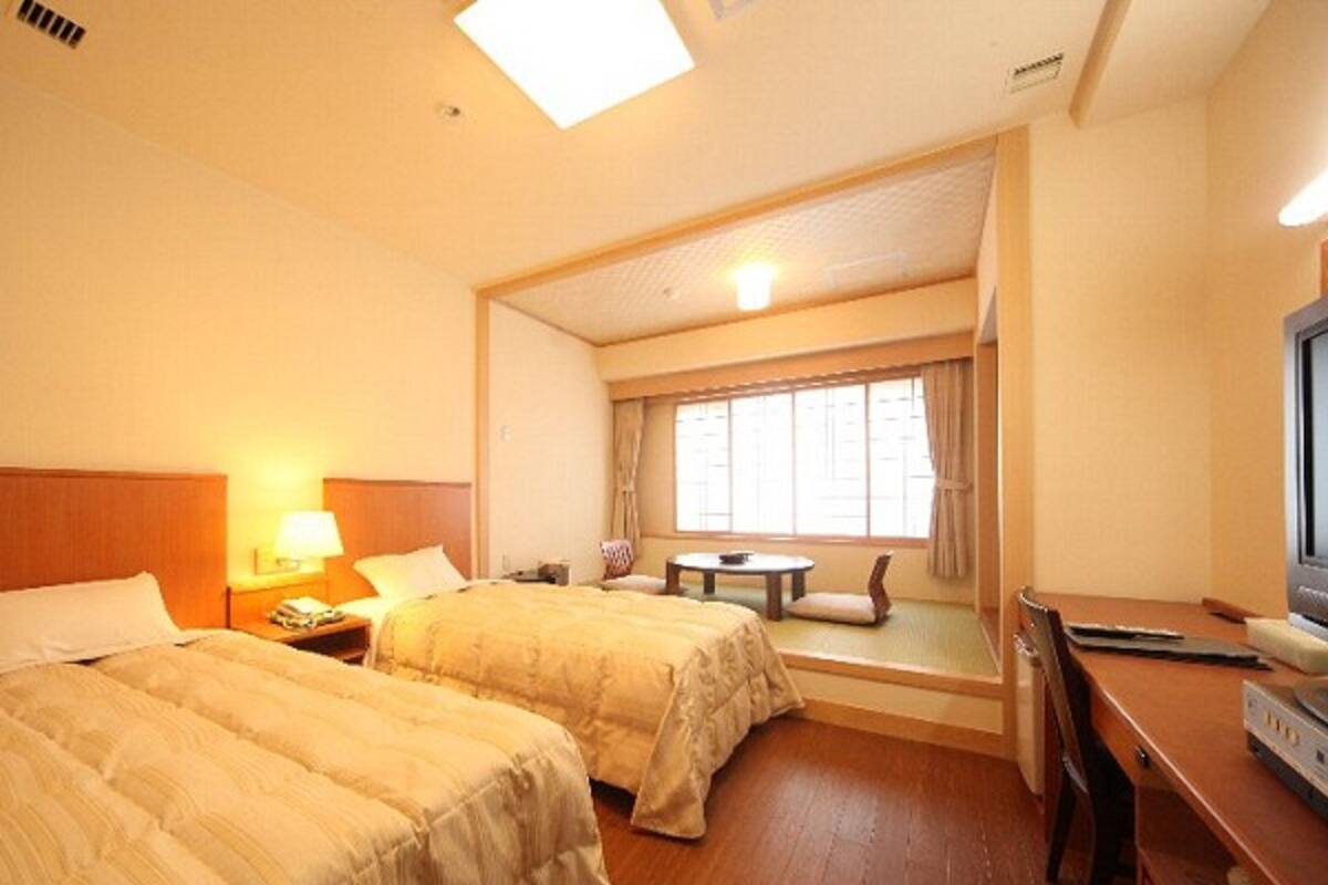 A hotel room with two beds, a desk, a television, and a window with curtains.