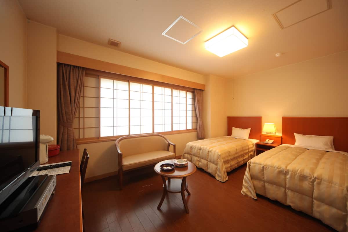 A hotel room with a bed, a desk with a computer, a chair, and a window with curtains.