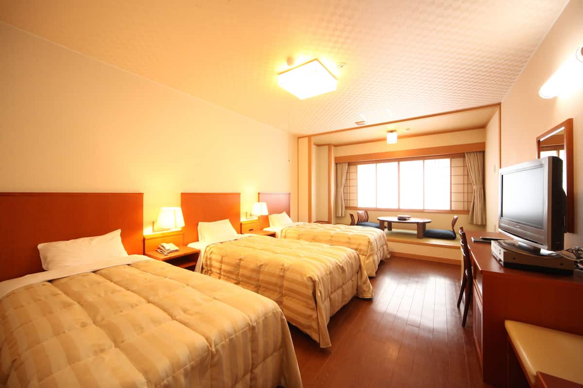 A hotel room with three beds, a television, a desk, and a window with curtains.