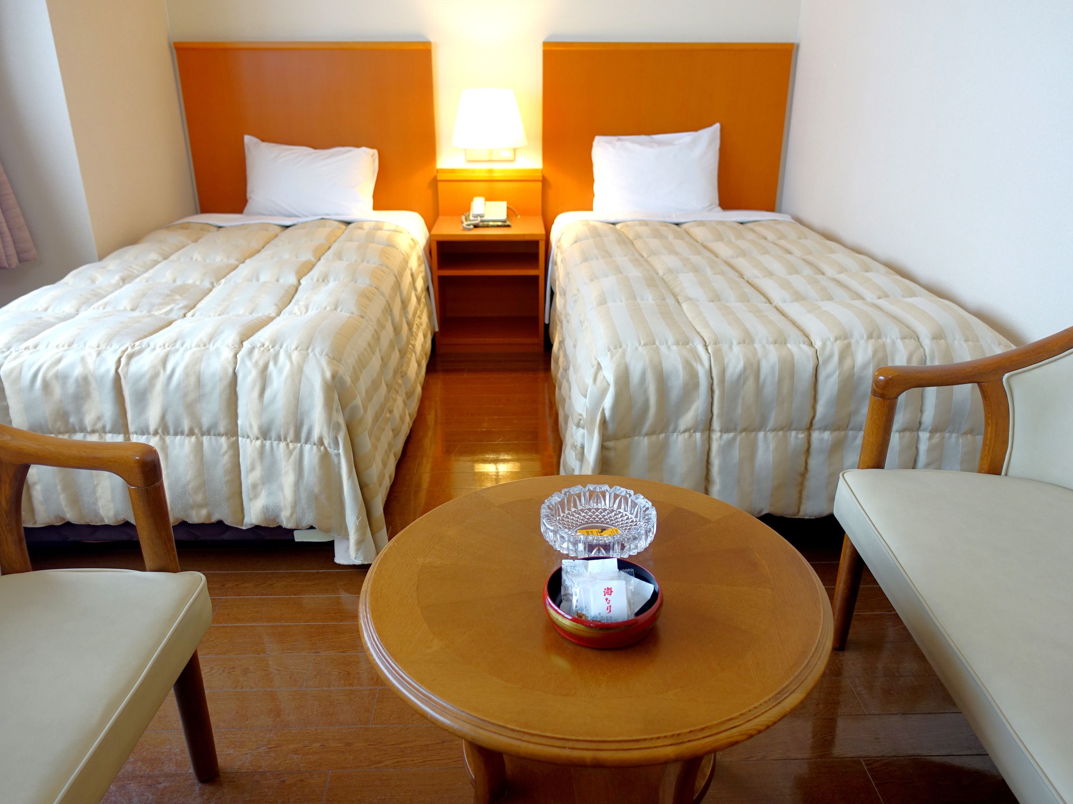 A hotel room with two beds, a nightstand, a table with a glass bowl, and wooden furniture.