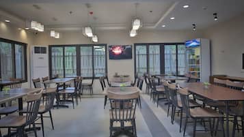 A spacious dining area with multiple tables and chairs, large windows, and a vending machine.