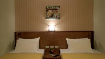 A hotel room with two beds, a wooden headboard, a wall-mounted artwork titled "OCEAN", and a nightstand with a remote control.