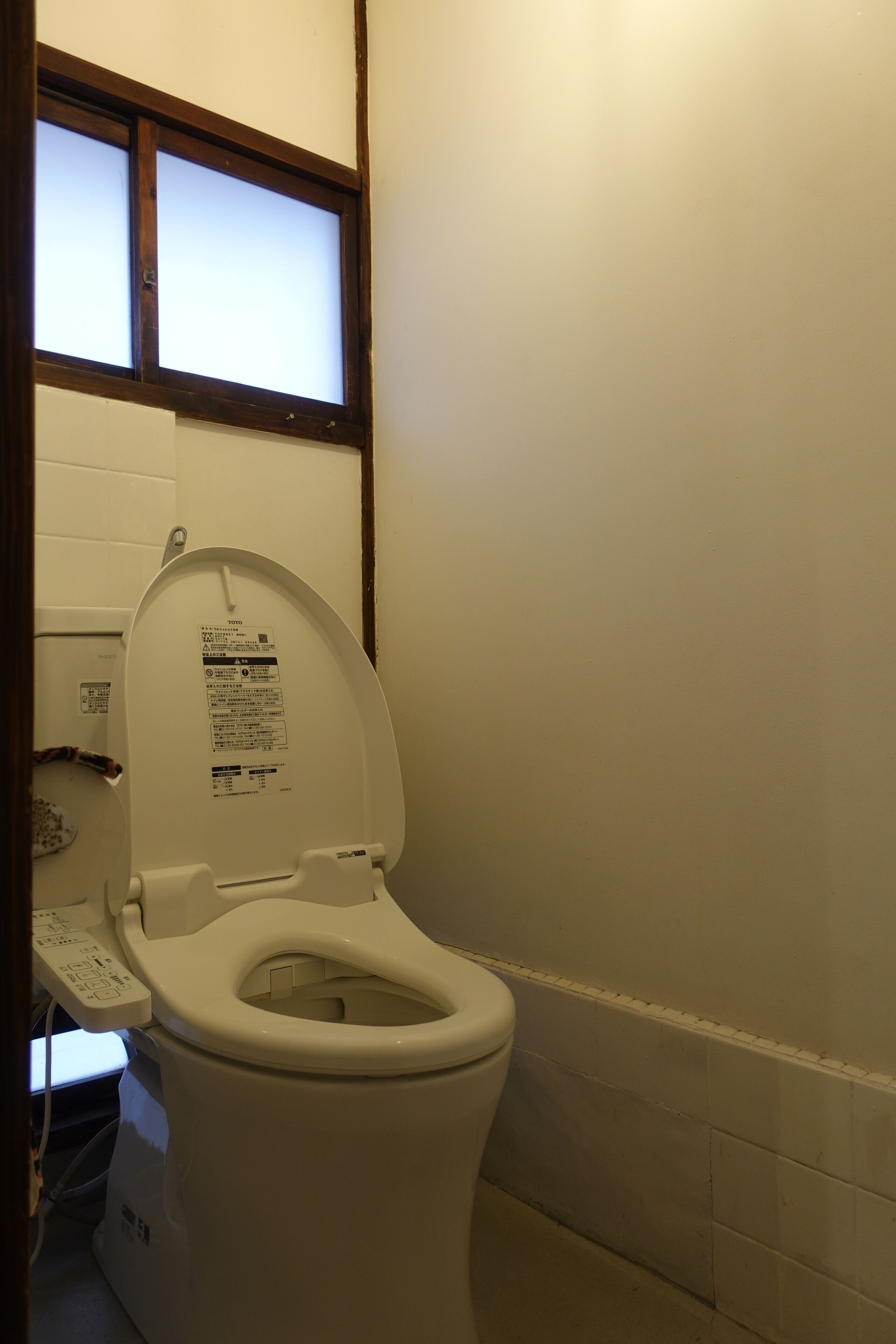 Un inodoro blanco con panel de control y una ventana encima.