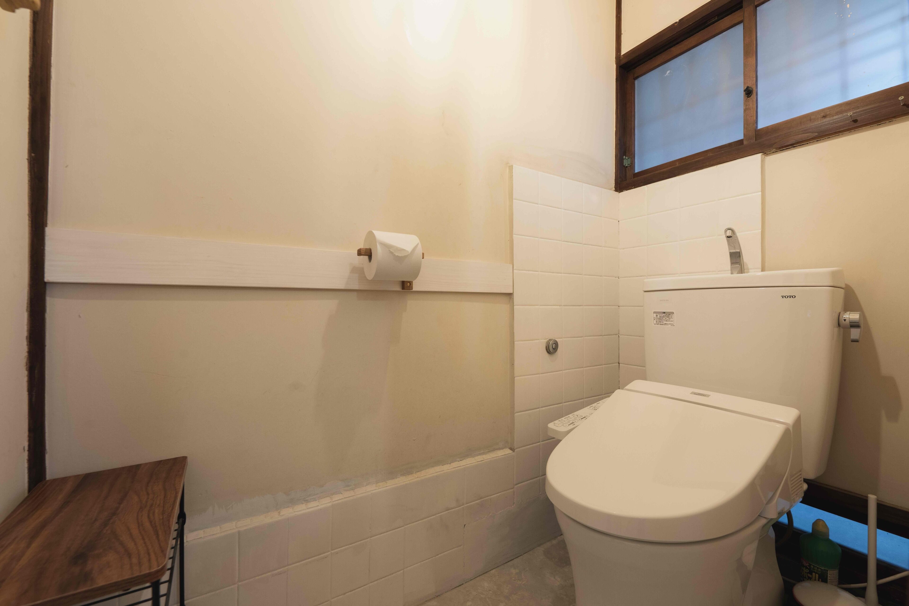 Un baño pequeño con inodoro, un taburete de madera y una ventana.