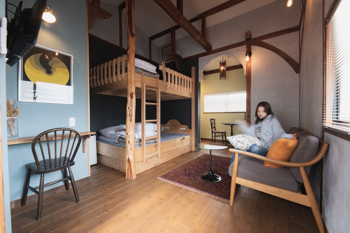 Um quarto com uma cama de solteiro e beliche, uma escrivaninha de madeira, uma cadeira e um sofá.