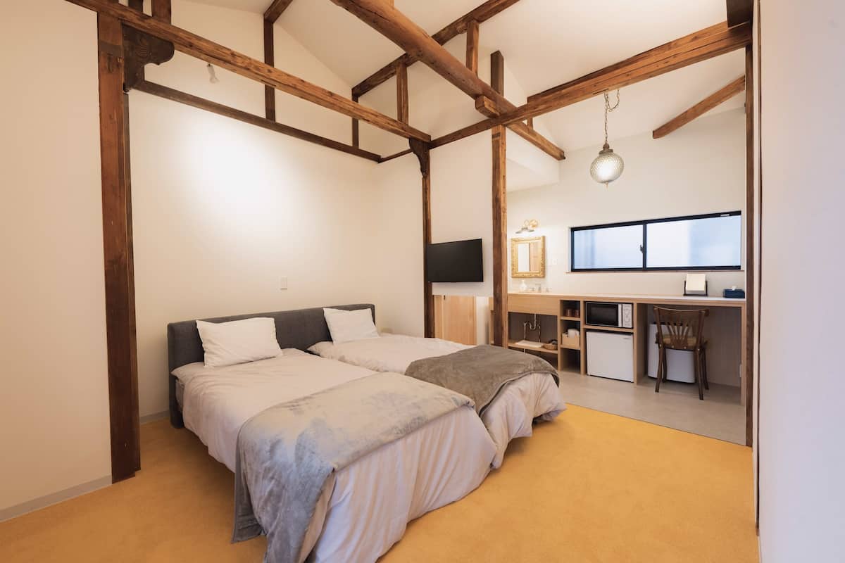 Quarto com duas camas, uma escrivaninha, uma cadeira, uma televisão e uma janela.