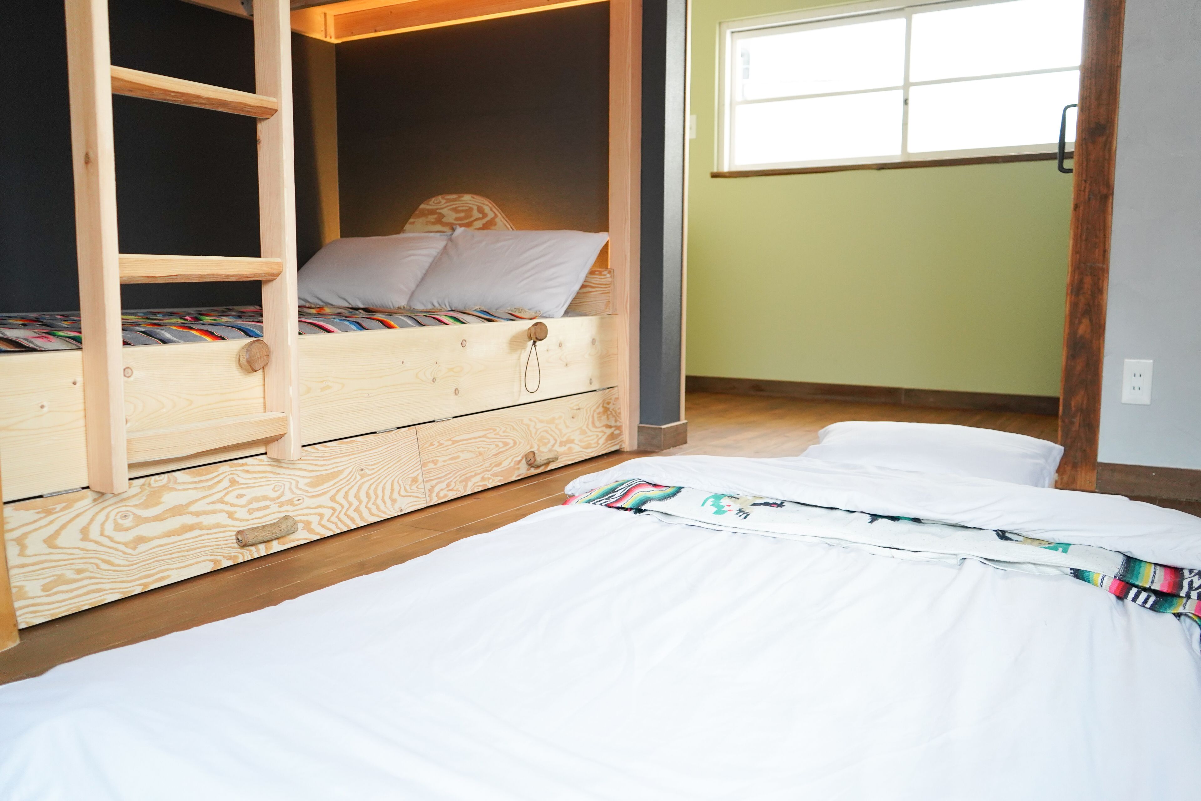 A bunk bed with a ladder, a wooden dresser, and a window with blinds.