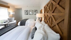 A hotel room with a large bed, a wooden headboard, a desk with a lamp, a chair, and artwork on the wall. - Saxon Inn (Alfred)