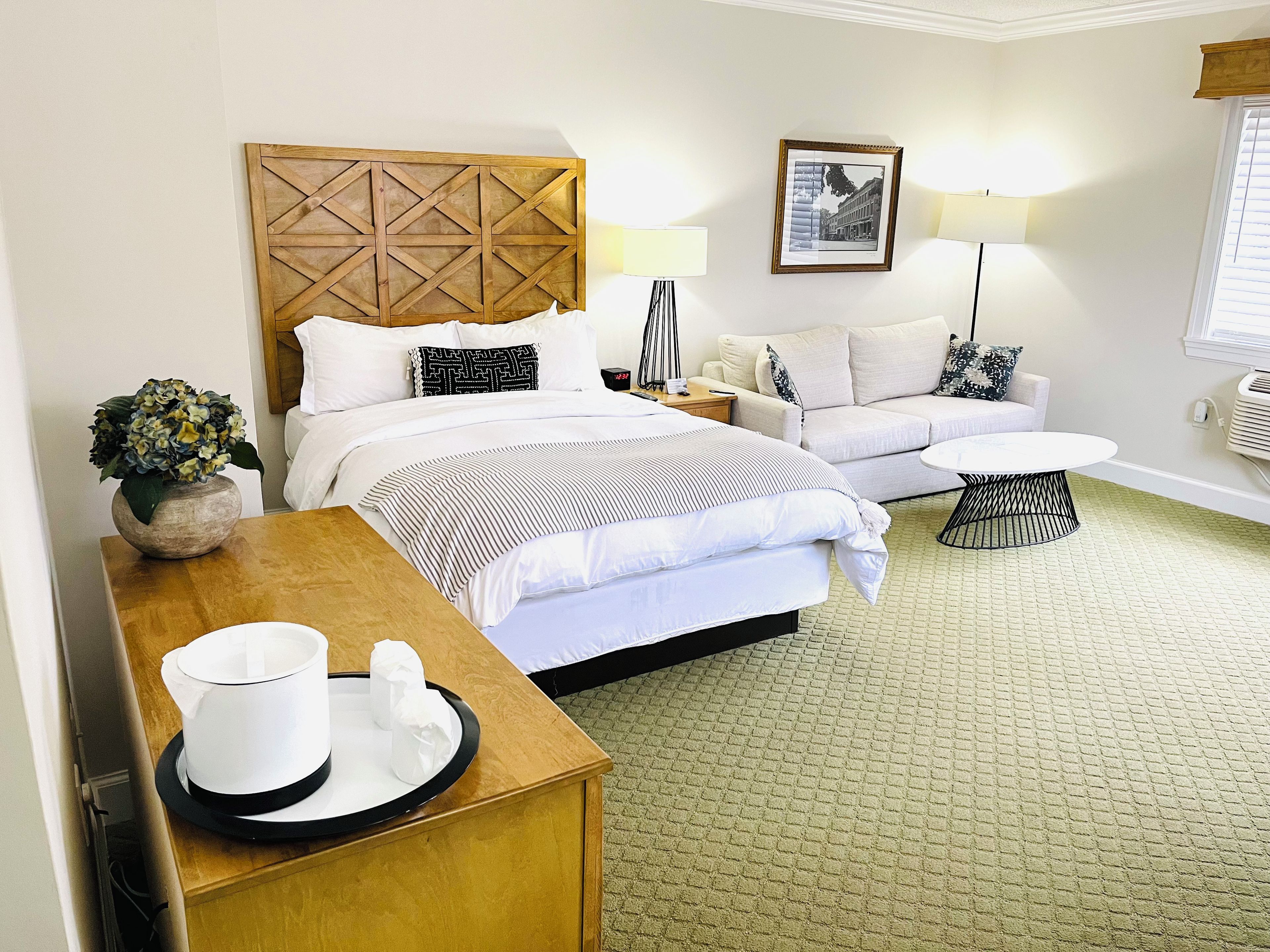A hotel room with a bed, a sofa, a small table, a lamp, and a picture on the wall.