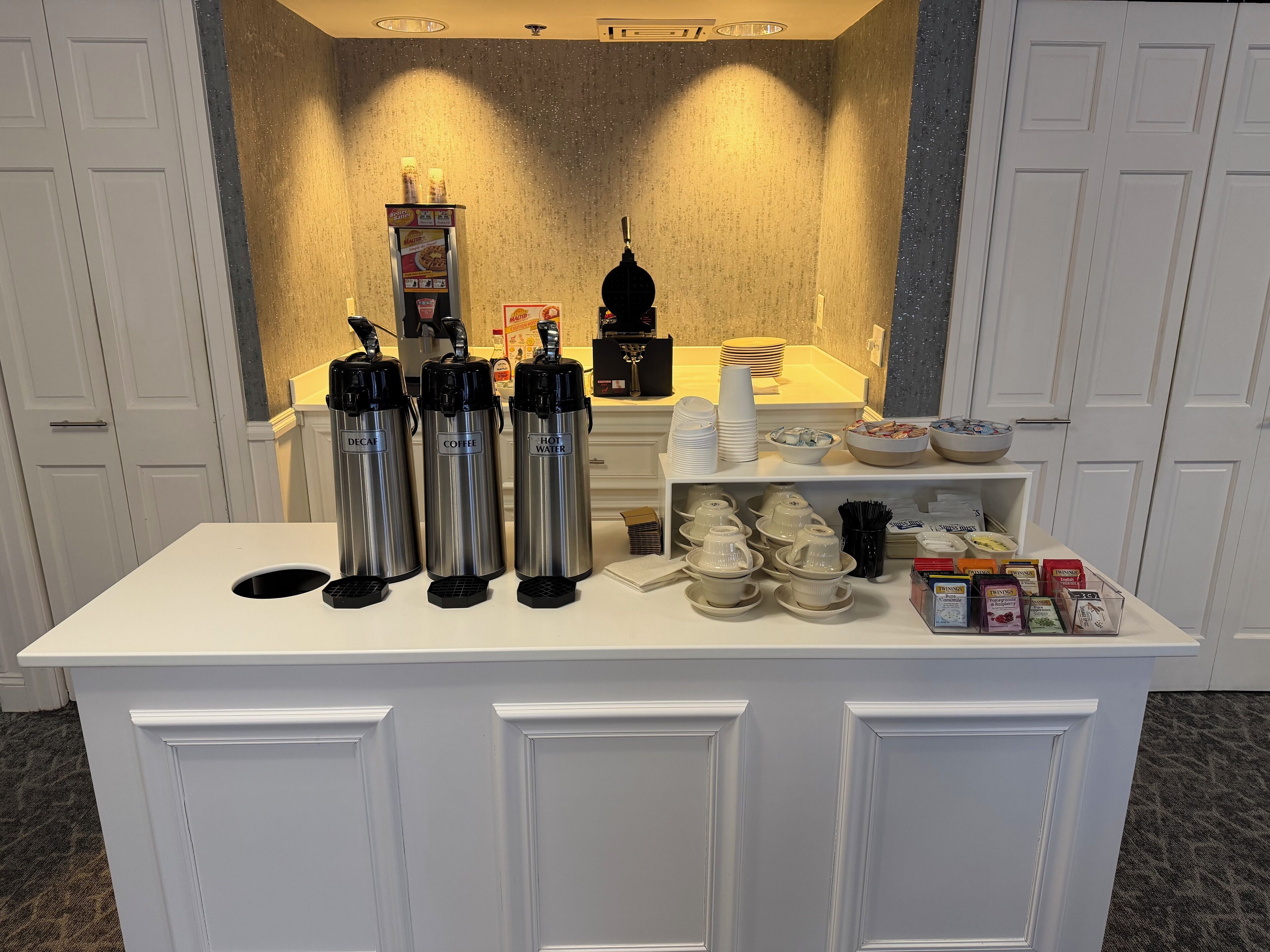 A self-service beverage station with three stainless steel dispensers labeled 'Decaf', 'Coffee', and 'Hot Water'.