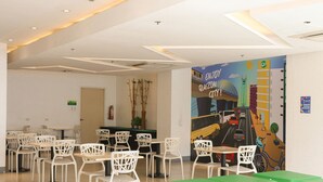 A modern dining area with white chairs and tables, a green seating area, and a mural on the wall. - Go Hotels North Edsa (Quezon City)