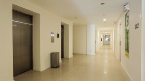 A clean, modern hotel corridor with an elevator, a trash bin, and a long hallway leading to a door at the end. - Go Hotels North Edsa (Quezon City)