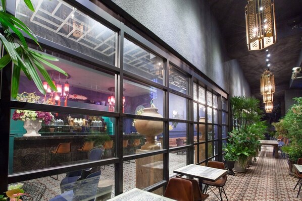 An indoor dining area with tables and chairs, large windows, and hanging lights.