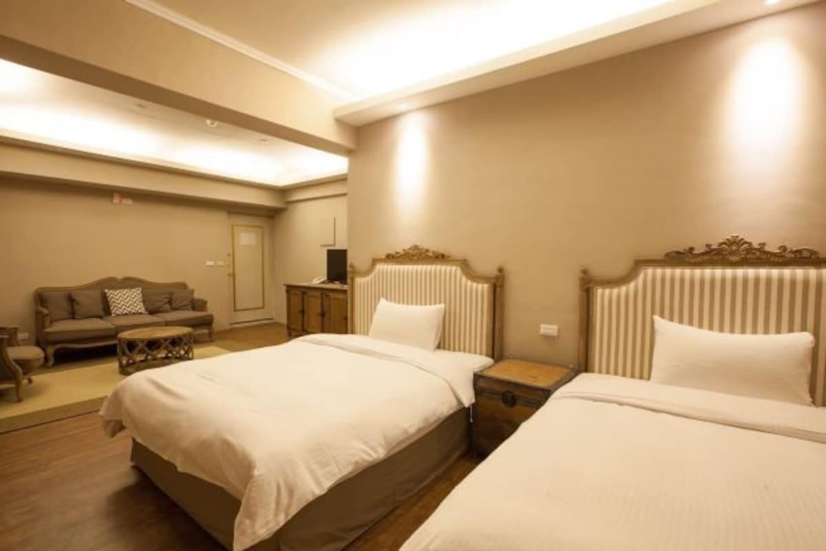 A hotel room with two beds, a sofa, a small table, and a nightstand.