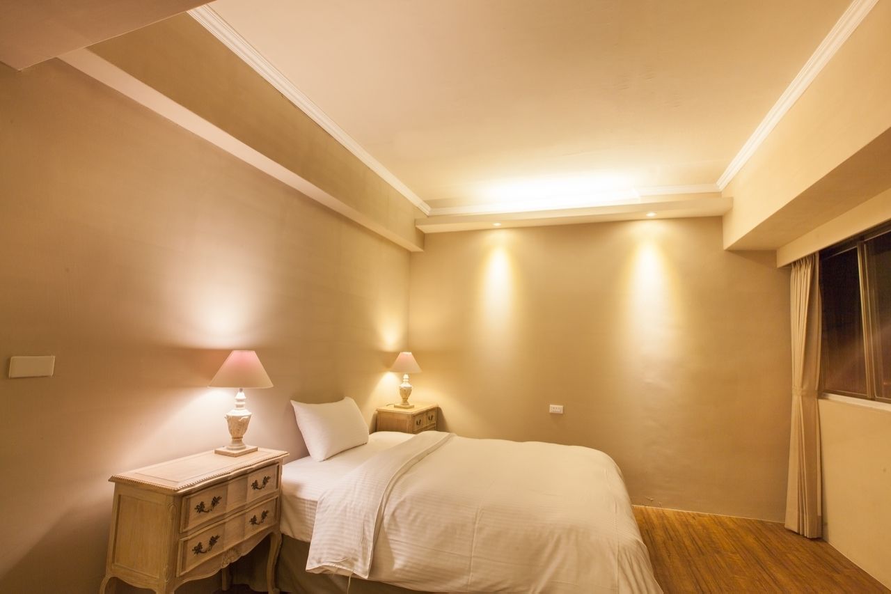 A bedroom with a bed, two bedside tables with lamps, a nightstand, and a window with curtains.