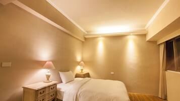 A bedroom with a bed, two bedside tables with lamps, a nightstand, and a window with curtains.