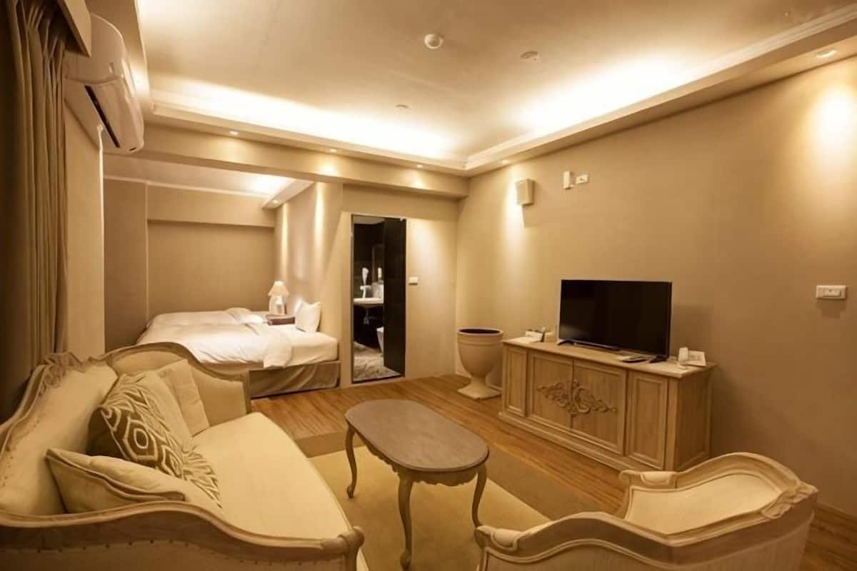 Una habitación de hotel con una cama, un sofá, un televisor, una mesita y un armario.