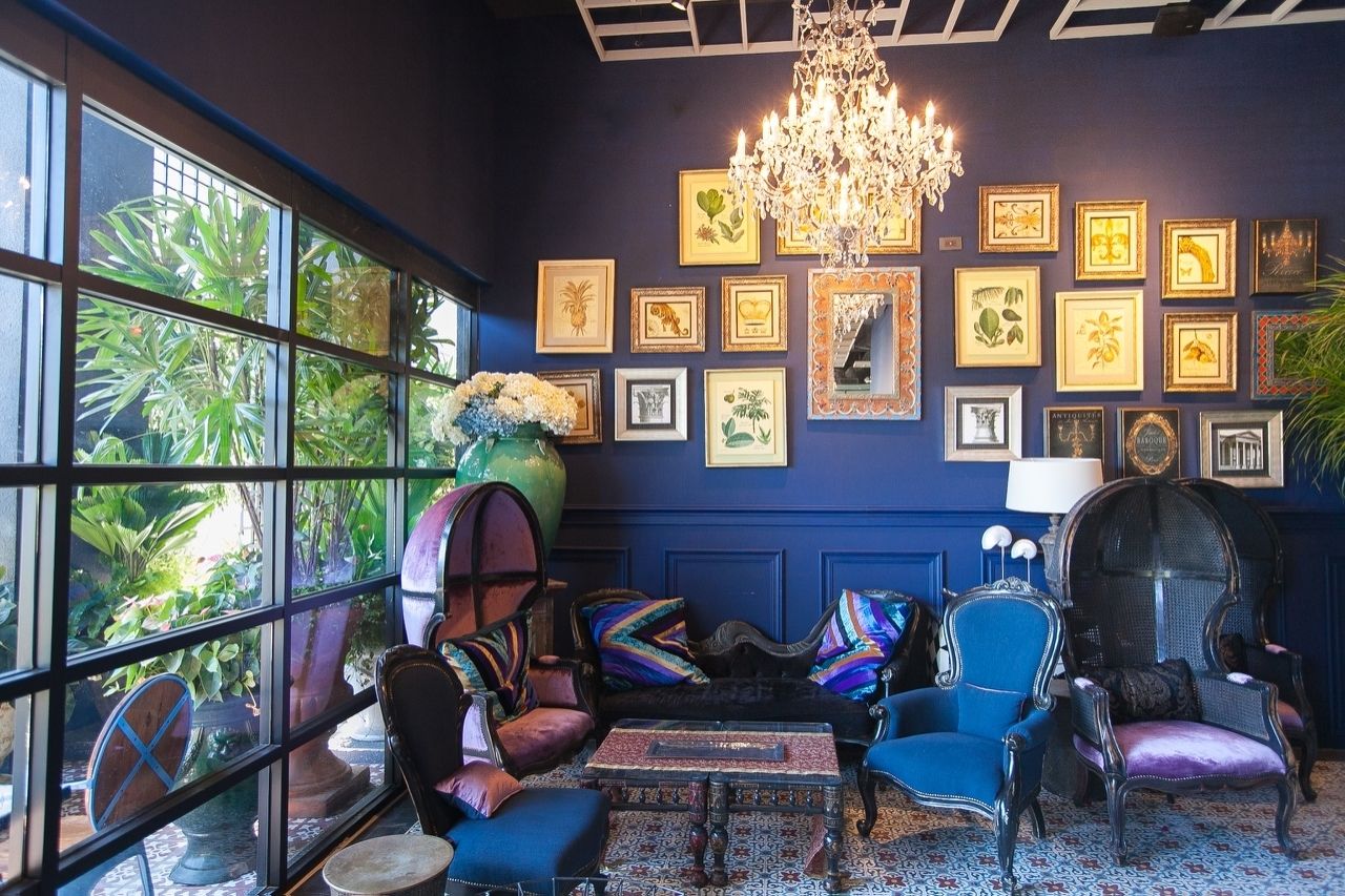 Una habitación con un ventanal grande, una araña y una pared decorada con grabados botánicos enmarcados.