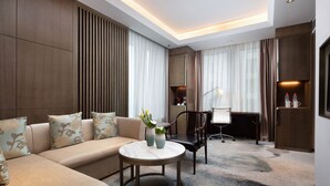 Ein modernes Hotelzimmer mit einer Couch, einem kleinen runden Tisch, einem Schreibtisch mit Stuhl und einem Fernseher.