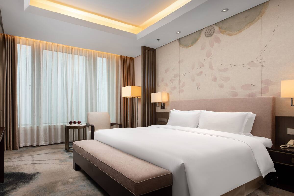 Quarto de hotel com uma cama grande, uma escrivaninha, uma cadeira e uma televisão.