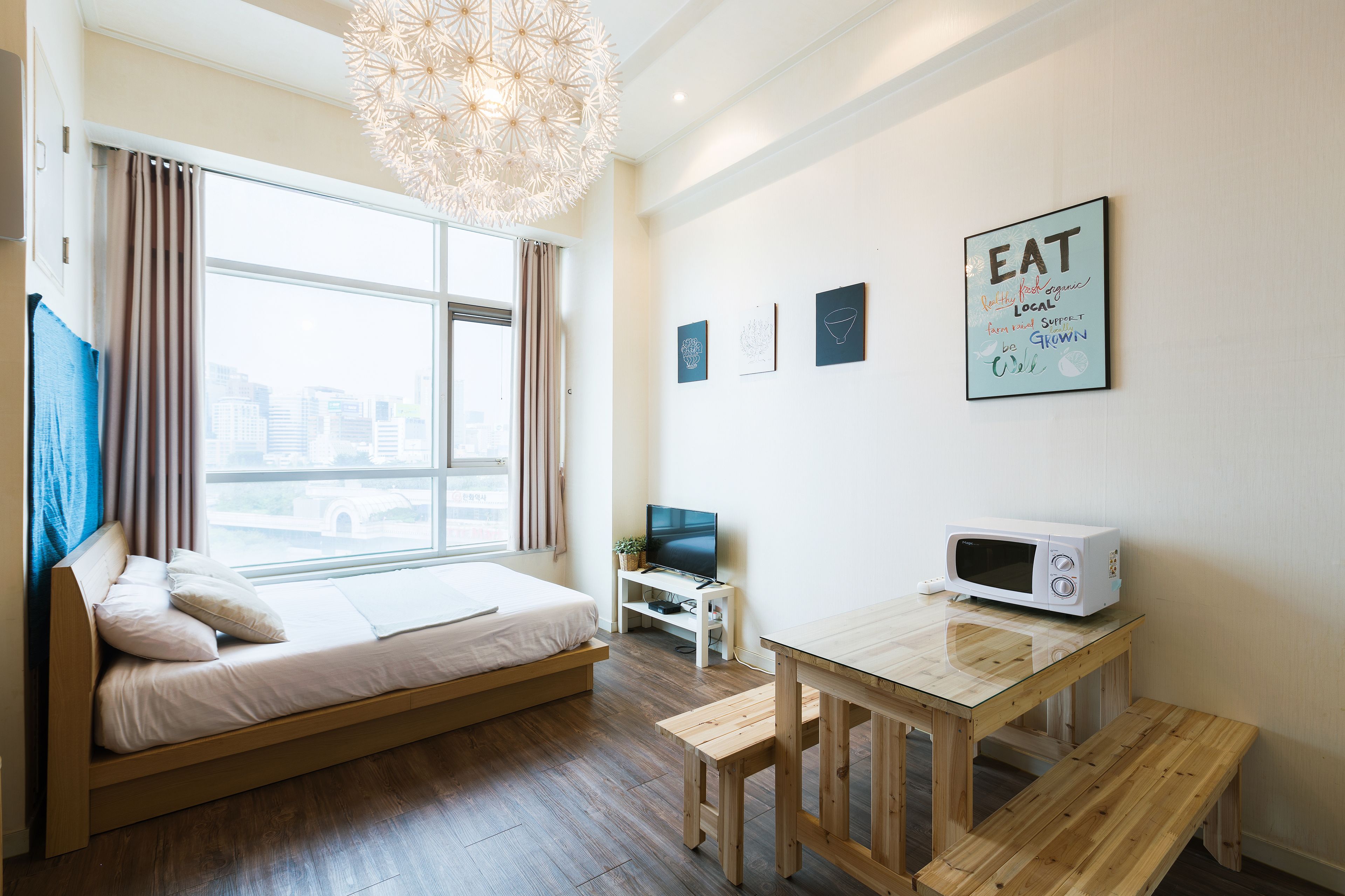 A modern room with a bed, a TV, a microwave, and a dining table.