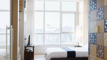 A bedroom with a large window, a bed, a desk with a computer, and a hanging basket.