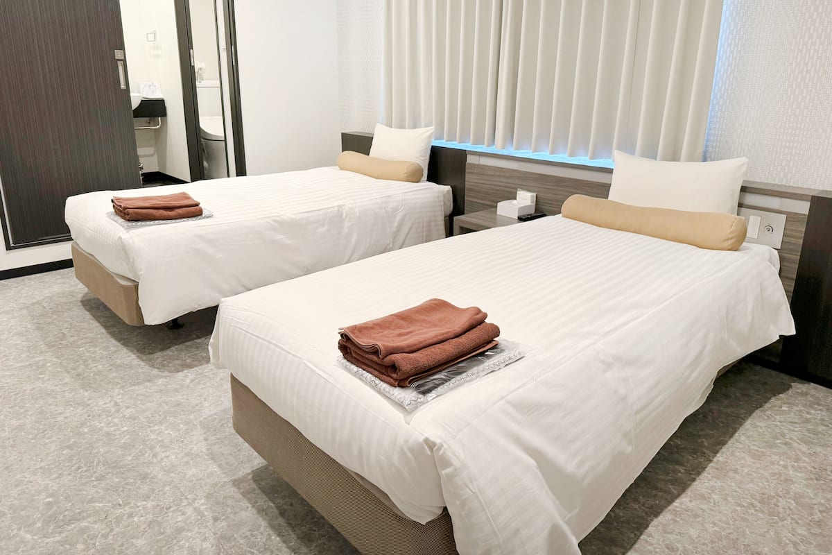Quarto de hotel com duas camas, cada uma com colcha branca e toalhas castanhas.