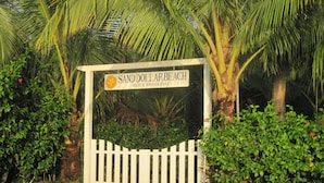 A sign for Sand Dollar Beach Bed & Breakfast surrounded by lush greenery and a white picket fence. - Sand Dollar Beach Bed & Breakfast (Bocas del Toro)