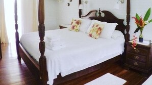 A four-poster bed with white linens, a wooden headboard, and floral pillows. - Sand Dollar Beach Bed & Breakfast (Bocas del Toro)