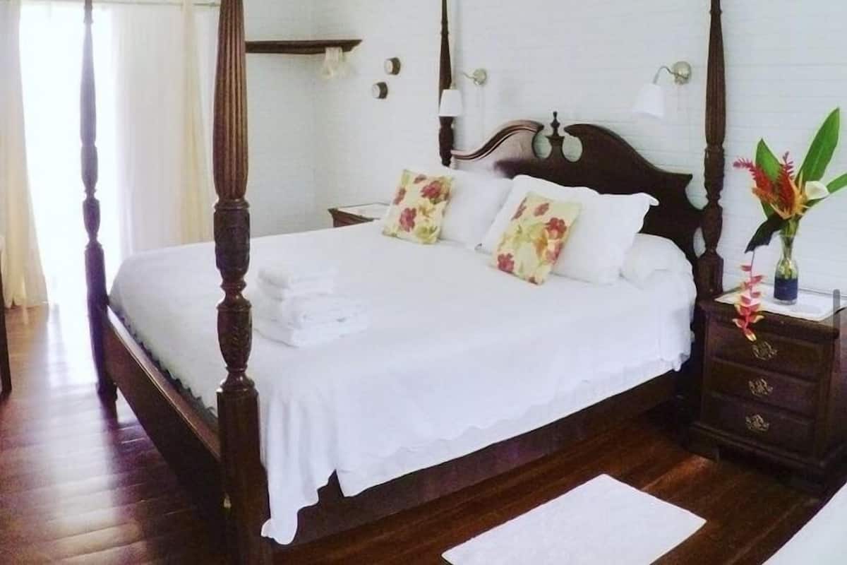 A four-poster bed with white linens, a wooden headboard, and floral pillows.