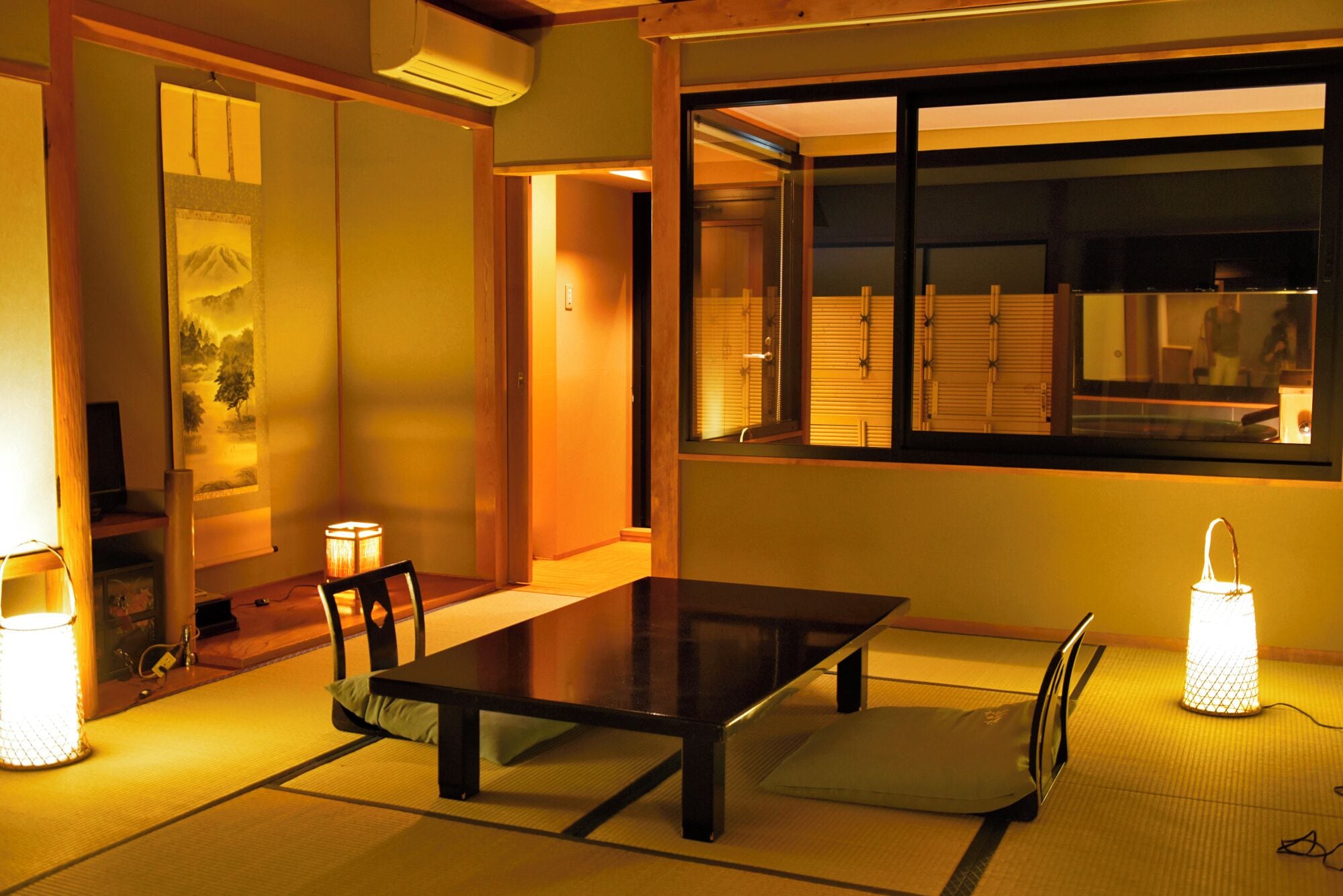 Ein traditioneller japanischer Raum mit Tatami-Boden, einem niedrigen Tisch, Stühlen und einer Schiebetür.