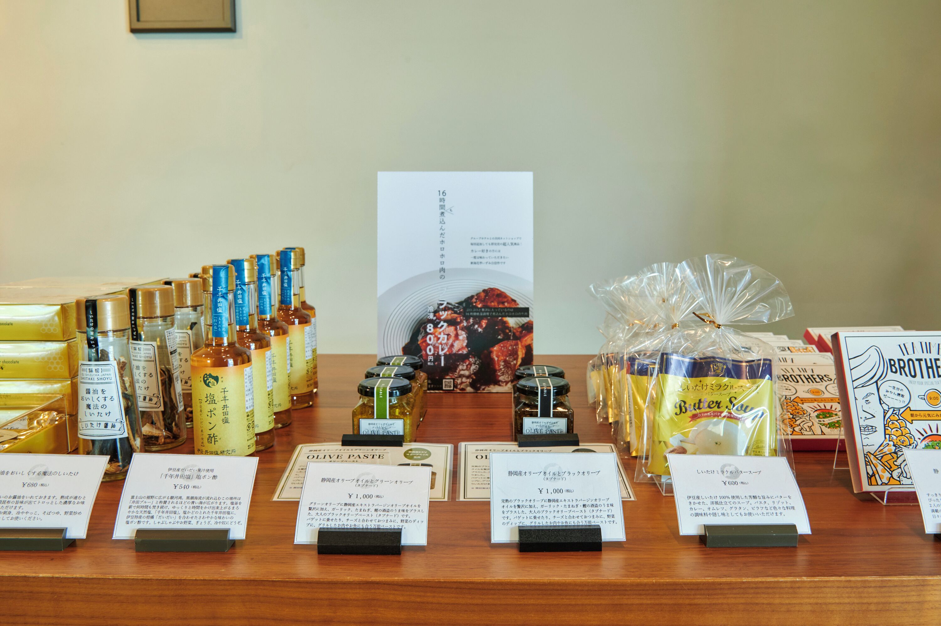 A display of various food products including olive oil, sauces, and packaged goods, with price tags and descriptions in Japanese.