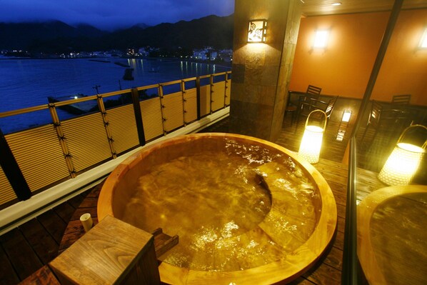 A hot tub with a wooden bench and a view of a body of water at night. - Shin-Kaikatei Izumi (Izu)