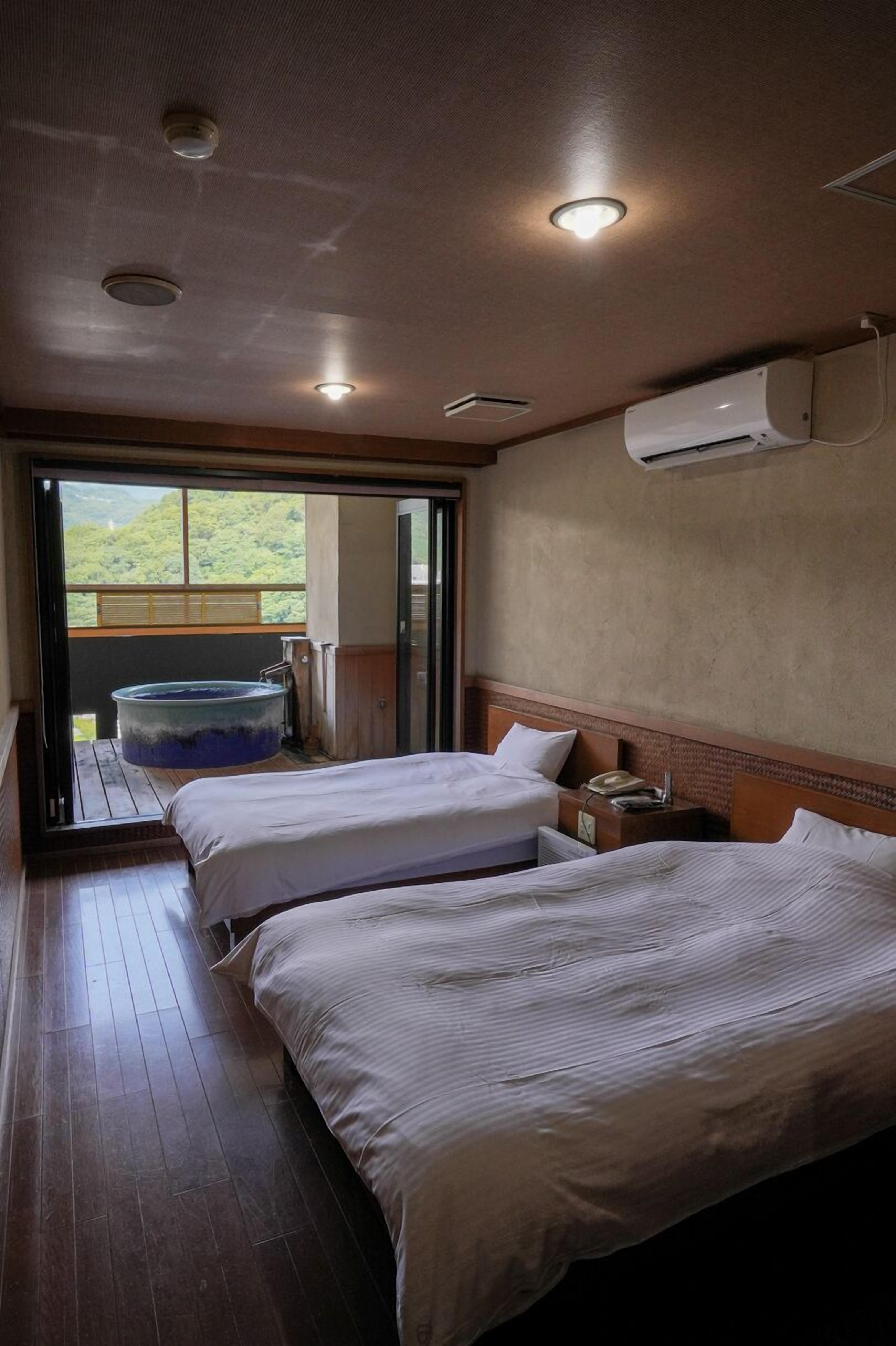 Ein Zimmer mit zwei Betten, Holzboden, Klimaanlage und Blick ins Grüne.