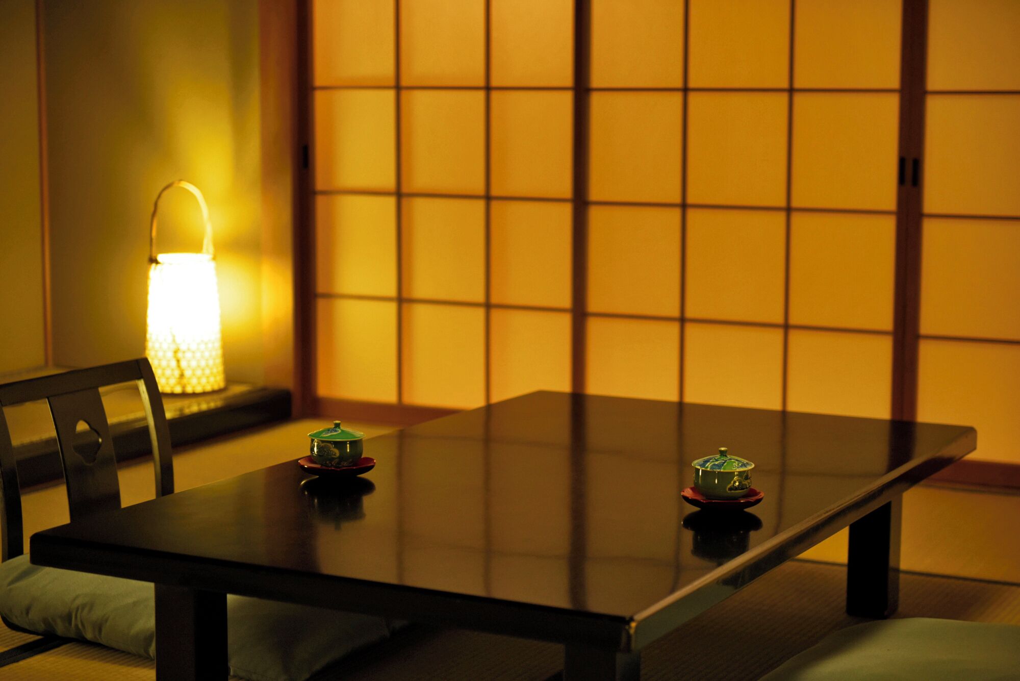 Una habitación tradicional japonesa con suelo de tatami, una mesa baja y un panel shoji al fondo.