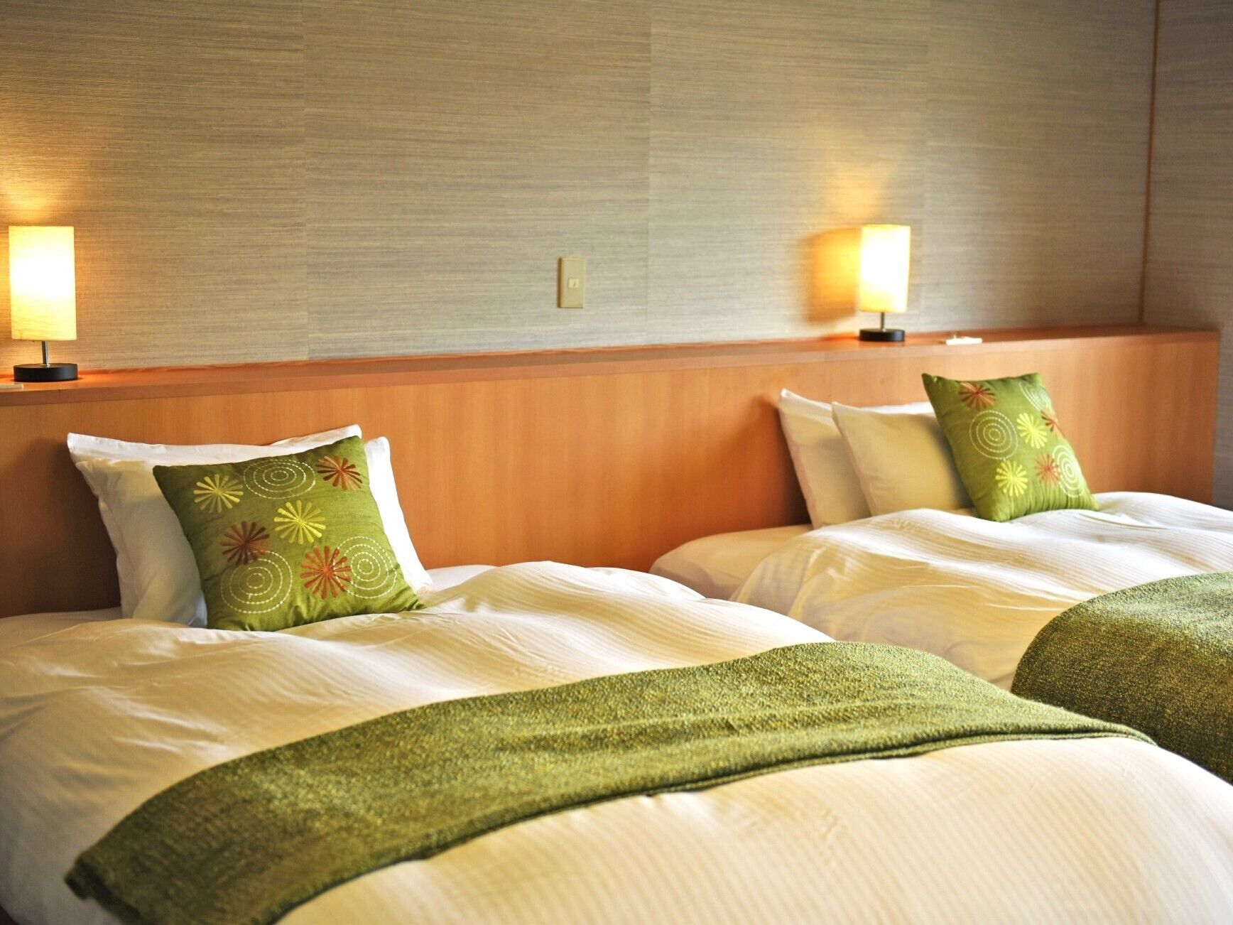 Ein Hotelzimmer mit zwei Betten, jedes mit einem grünen Kissen, einem hölzernen Kopfteil und zwei Wandlampen.
