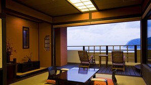 Una habitación con esteras de tatami, una mesa baja y sillas. Se ve el mar a través de amplios ventanales.