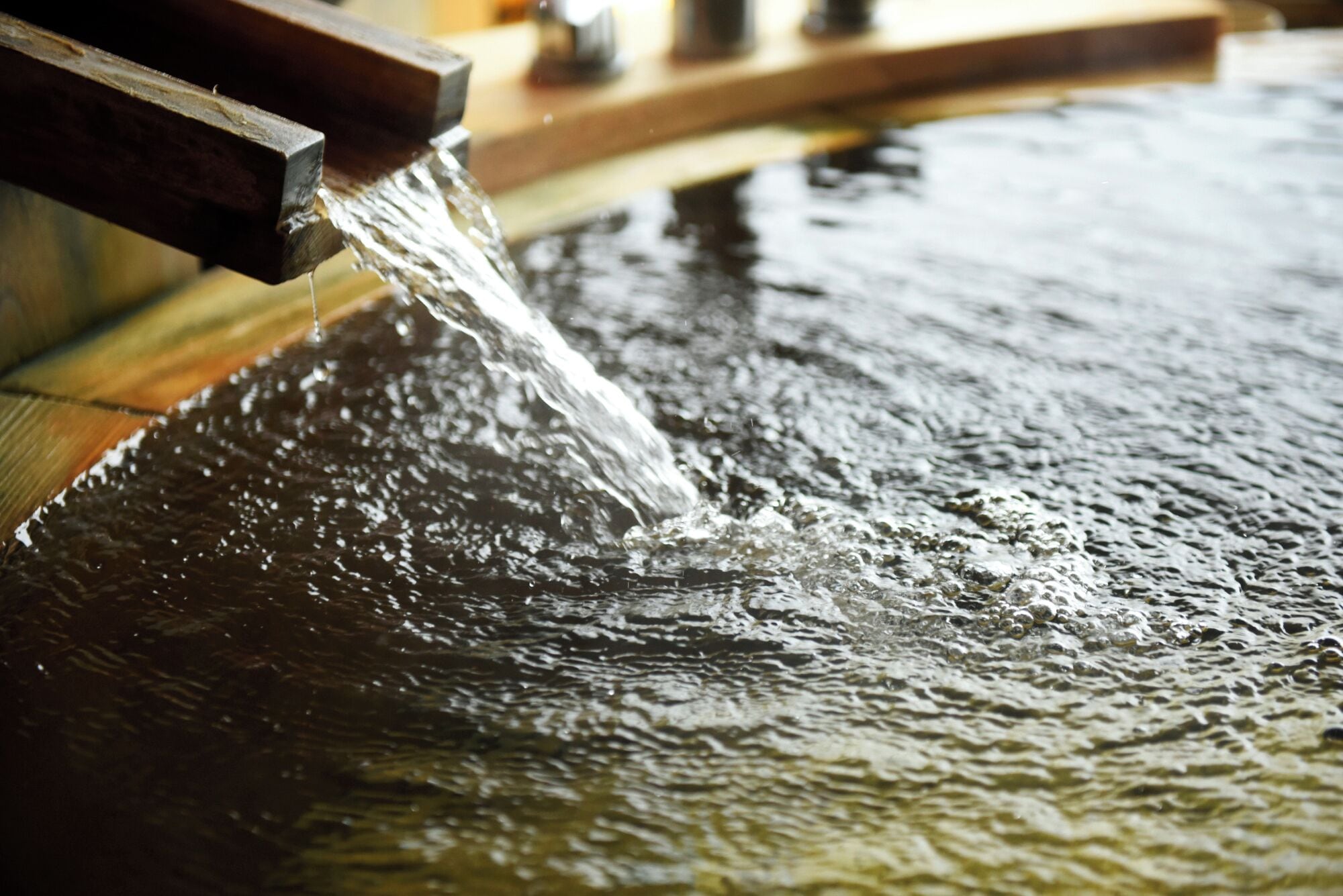 A close-up of water flowing from a wooden structure into a reflective surface.